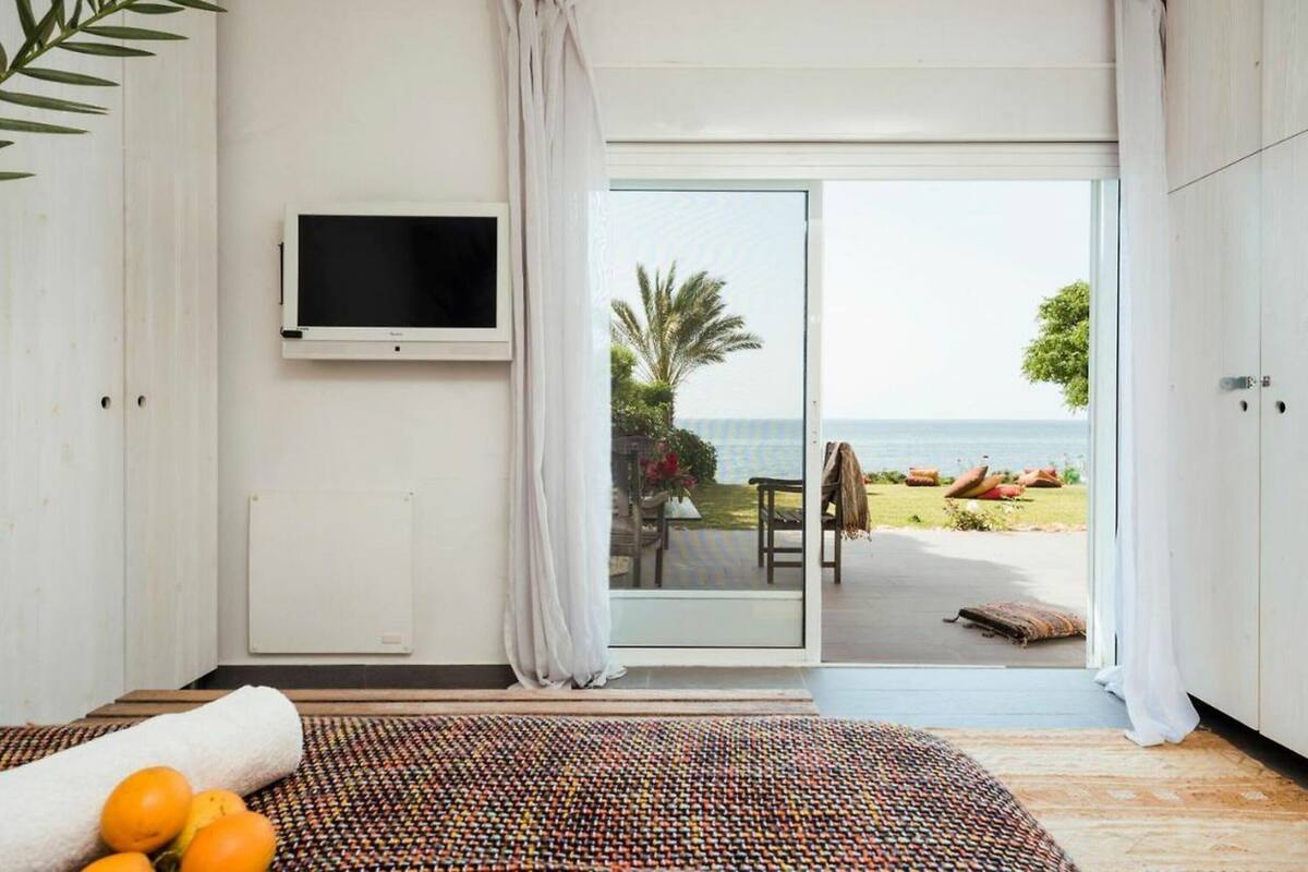 A bedroom with a bed, a television, a view of the beach, and a sliding glass door.