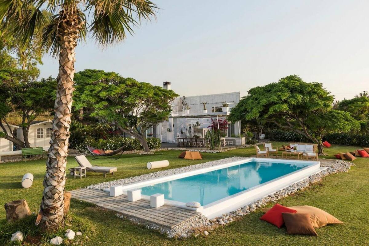 A rectangular pool with a white edge, surrounded by a pebble border, with lounge chairs and a dining area in the background.