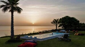 A pool area with lounge chairs and a palm tree, overlooking a calm sea at sunset. - Villa Koki Zantos Sea View  (Zakynthos)