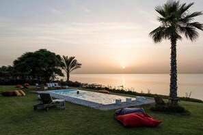 A pool area with lounge chairs and a palm tree, overlooking a body of water at sunset. - Villa Koki Zantos Sea View  (Zakynthos)