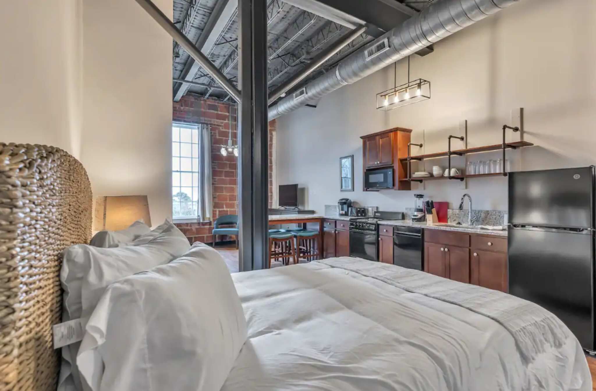 A modern hotel room with a large bed, a kitchenette, and a view of the city.
