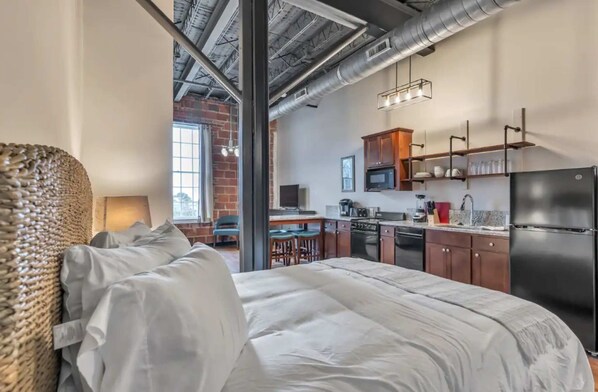 A modern hotel room with a large bed, a kitchenette, and a view of the city.