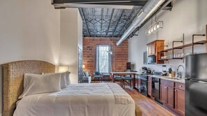 Ein Zimmer mit Bett, Küchenzeile und Backsteinwand.