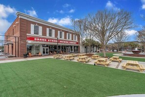 A brick building with a sign reading "Grand Strand Brewing Company." There are outdoor picnic tables and a fountain in the background. - Beach Brews & Coastal Views Loft (Myrtle Beach)