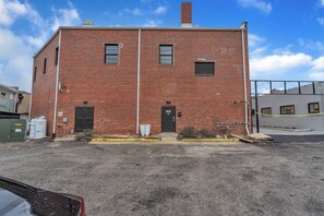 A two-story brick building with a black door and windows, a gravel driveway, and a fenced area. - Beach Brews & Coastal Views Loft (Myrtle Beach)