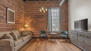 A cozy living room with a brick wall, a sofa, two chairs, a small table, a TV, and a dresser. - Beach Brews & Coastal Views Loft (Myrtle Beach)