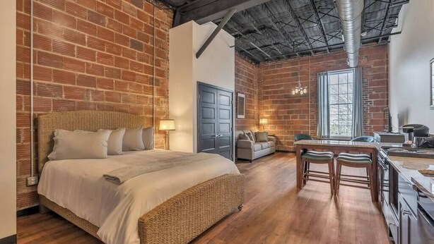 A spacious bedroom with a large bed, a dining area with two stools, and a kitchen area. - Beach Brews & Coastal Views Loft (Myrtle Beach)