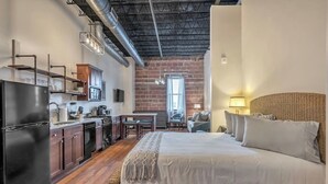 A compact hotel room with a kitchenette, a large bed, and a brick wall.