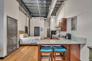 A compact hotel room with a bed, a kitchenette, and a small bar area.