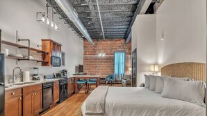 Een kleine hotelkamer met kitchenette, een bed en een eethoek.