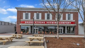 A brick building with a red awning labeled "GRAND STRAND BREWING COMPANY". - Sip, Stay, Play  Loft Above a Brewery (Myrtle Beach)