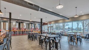 A spacious restaurant with high ceilings, industrial-style lighting, and large windows offering a view of the outdoors. - Sip, Stay, Play  Loft Above a Brewery (Myrtle Beach)