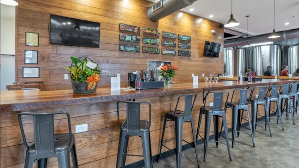 A modern bar area with a wooden wall, multiple bar stools, and a long counter. - Sip, Stay, Play  Loft Above a Brewery (Myrtle Beach)