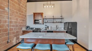A kitchen with a central island, bar stools, a microwave, a refrigerator, and a hanging light fixture. - Sip, Stay, Play  Loft Above a Brewery (Myrtle Beach)