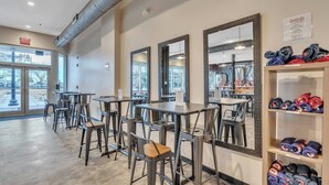 Un espacio interior moderno con mesas y sillas de metal, espejos grandes y un perchero con objetos doblados a la derecha.