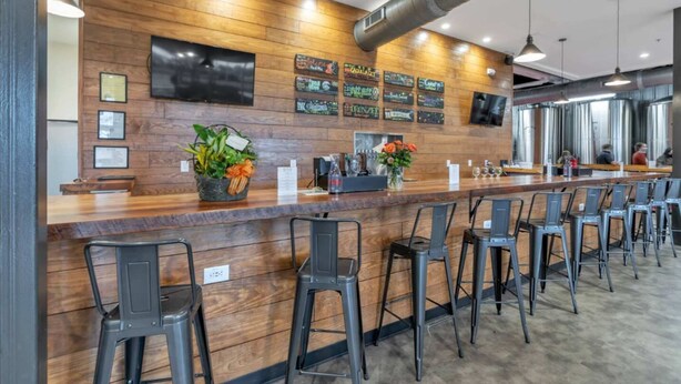 Zona de bar con paneles de madera, varios taburetes, una barra con dispensador de bebidas y un televisor montado en la pared.