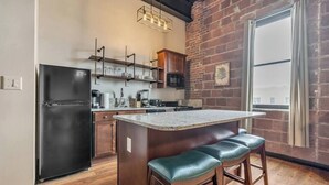 A modern kitchen with a black refrigerator, wooden cabinets, a granite countertop, and a brick wall.
