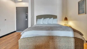 A bedroom with a bed, a bedside lamp, a door, and a framed picture on the wall.