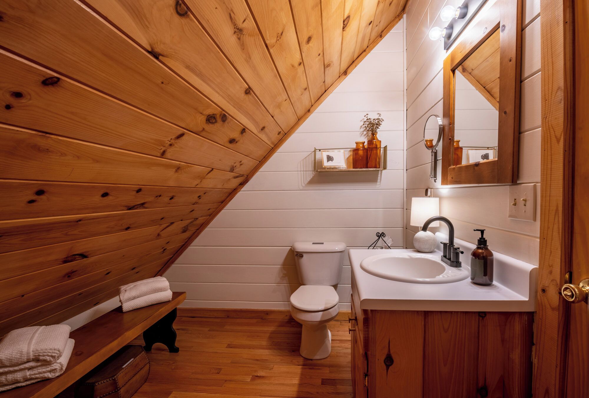 Een betegelde badkamer met een bankje, toilet en wastafel.
