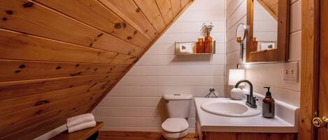 Een betegelde badkamer met een bankje, toilet en wastafel.