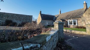 A stone building with a traditional design, featuring a stone wall, a grassy lawn, and a clear blue sky.