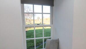 A window seat with a cushion, a view of a grassy yard, and a white wall.