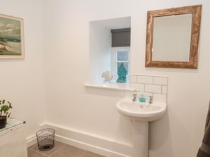 A bathroom with a white sink, a mirror, a window, and a Buddha statue. - Flodden (Cornhill on Tweed)