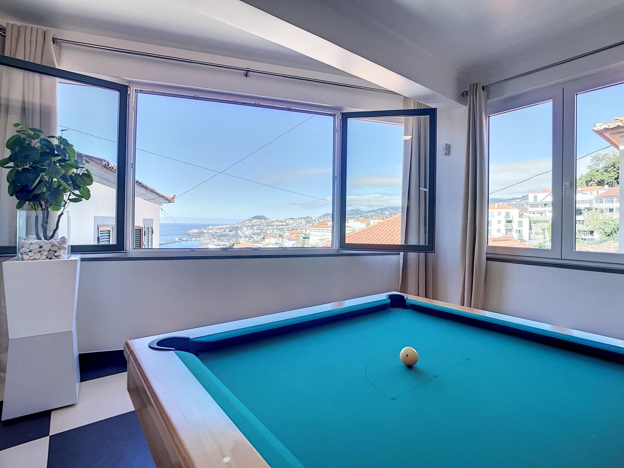 Una mesa de billar en una habitación con ventanales que ofrecen vistas a la ciudad.