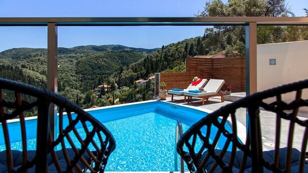 A swimming pool with two lounge chairs facing it, surrounded by a wooden fence and a view of a hilly landscape. - Villa Alba in Lefkada (Lefkada)