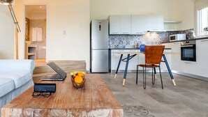 A modern kitchen with white cabinets, a microwave, and a refrigerator. There is a dining table with a chair and a bowl of fruit. - Villa Alba in Lefkada (Lefkada)