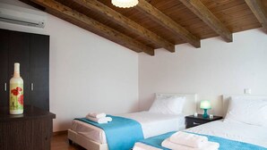 Une chambre d’hôtel avec deux lits, un plafond en bois, une armoire sombre et une table de chevet avec une lampe.