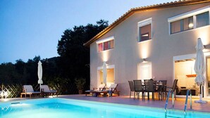 Un espace aménagé au bord de la piscine, avec des chaises longues et une table à manger, le tout entouré d’un bâtiment doté de nombreuses fenêtres et portes.