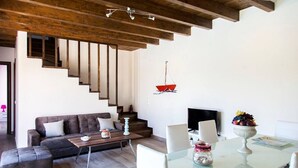 Un salon moderne avec un escalier, un coin repas doté d’une table en verre et un téléviseur fixé au mur.