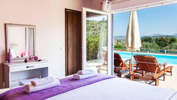 Une chambre dotée d’un grand lit, d’une coiffeuse avec des articles de toilette, d’une vue sur une piscine et d’une porte donnant sur un espace extérieur.