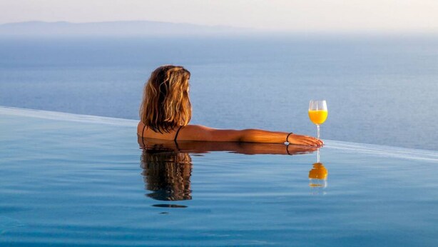 A person relaxing on a glass infinity pool with a glass of orange juice, overlooking a calm sea. - Syvota 08 Sunset 2B Zara (Igoumenitsa)
