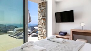 A hotel room with a bed, a TV, a stone wall, and a balcony with a view. - Syvota 08 Sunset 2B Zara (Igoumenitsa)