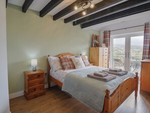 Un dormitorio con una cama de madera, una mesita de noche, un aparador y vistas por un ventanal grande.