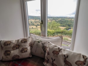 Asiento junto a la ventana con cojines estampados con motivos animales, con vistas a un paisaje rural.