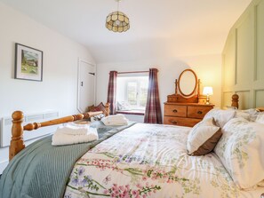 A bedroom with a bed, a dresser, a mirror, a window with curtains, and a hanging light fixture.