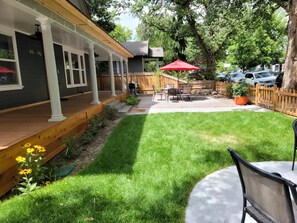 Un jardin avec une terrasse en bois, un patio couvert et un parasol rouge.