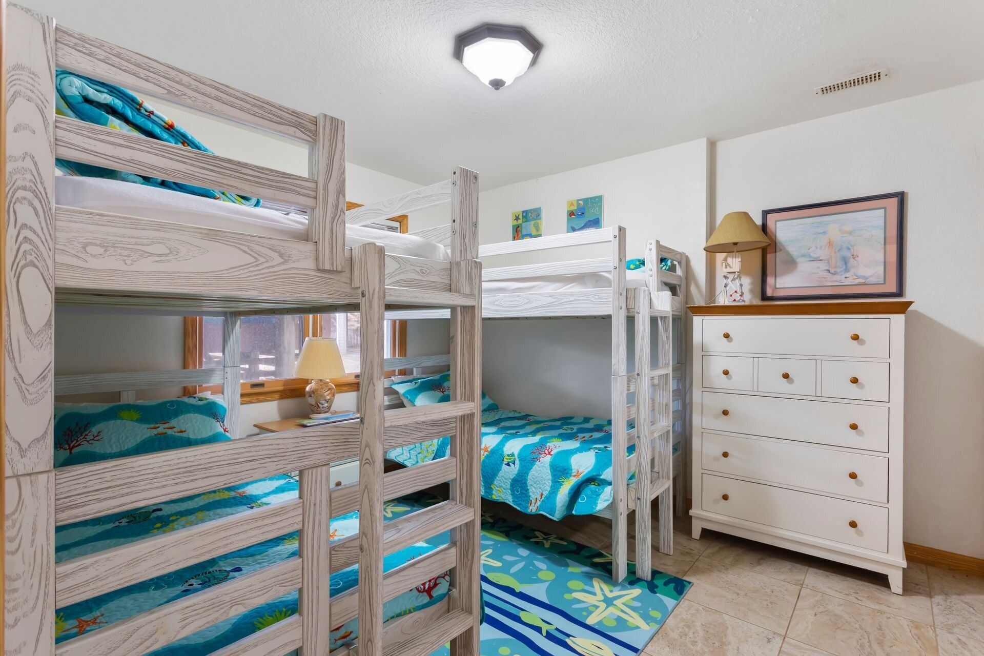 Une chambre d’enfant avec des lits superposés, une commode et une lampe.