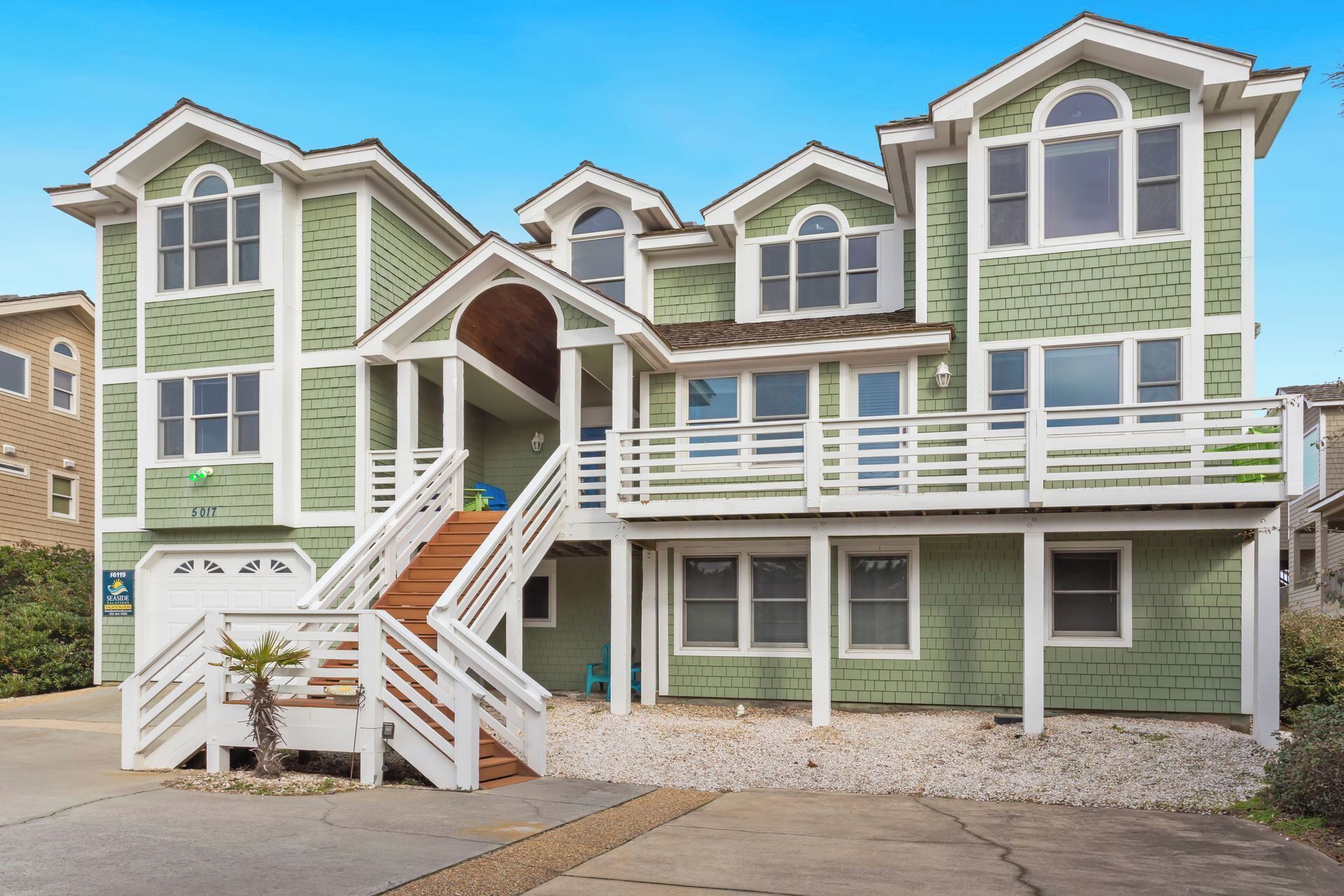 A multi-story house with a green exterior, white trim, and a front porch with a staircase.