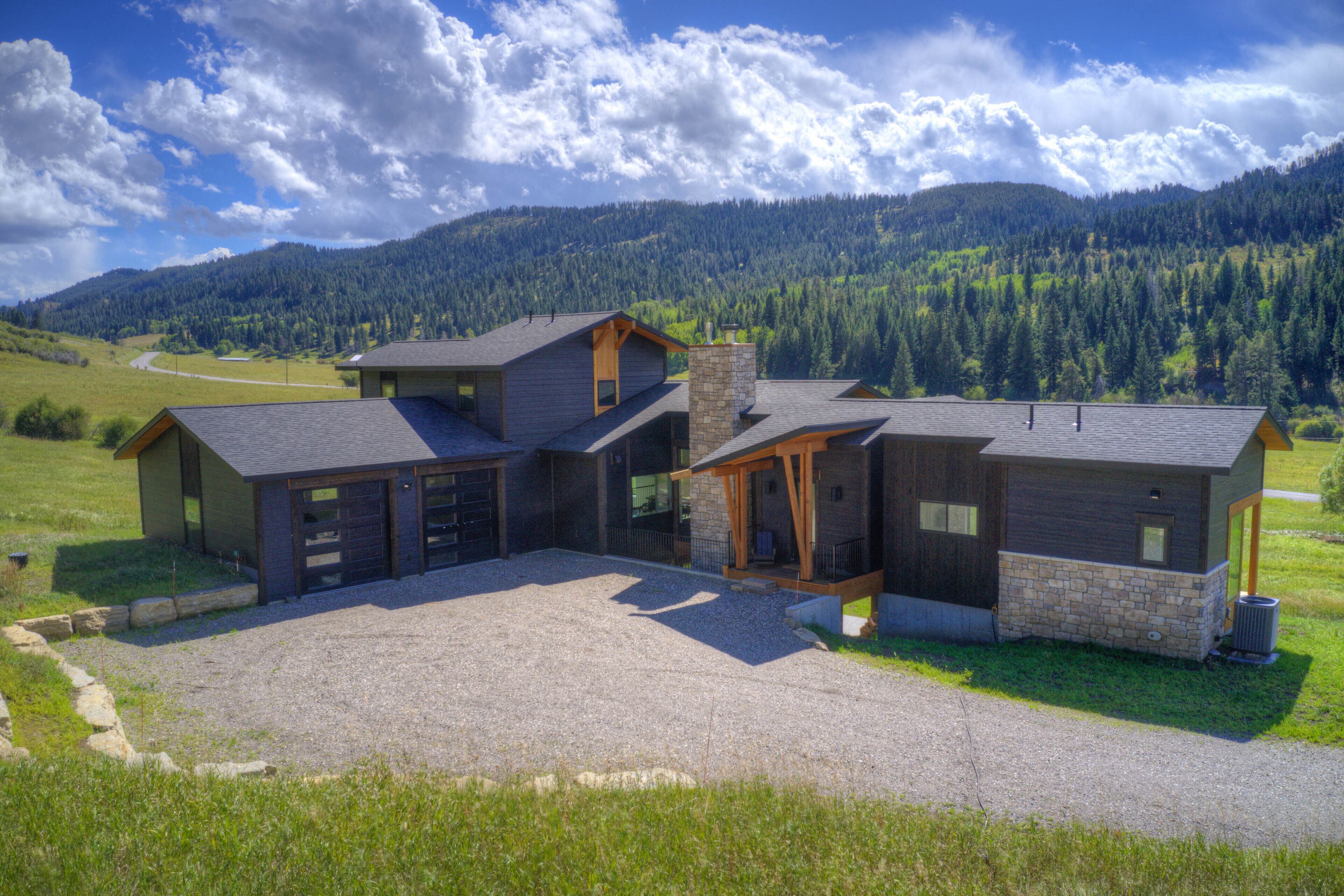 Una casa moderna con un ampio vialetto, ampie finestre e vista su una catena montuosa ricoperta di boschi.