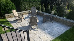 Eine Terrasse mit Adirondack-Stühlen, einem Tisch und einer Steinmauer.