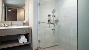A modern bathroom with a glass-enclosed shower, a vanity with a mirror, and neatly rolled towels on a shelf.