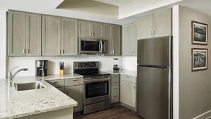 A modern kitchen with grey cabinets, stainless steel appliances, a granite countertop, and a wooden floor.