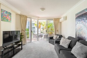 Relax in this stylish living room with a flat-screen TV, comfortable sofa, and a beautiful view from the sliding glass door leading to the outdoor balcony.