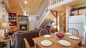 A cozy living room with a fireplace, a television, and a dining area with a table set for four. - Peaceful Cabin Near Many Activities (Beech Mountain)