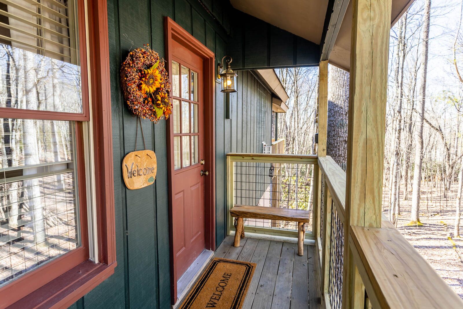 A wooden porch with a red door, a welcome sign, and a decorative wreath.