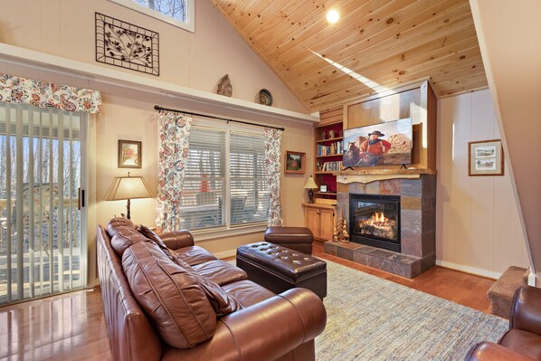 A cozy living room with a fireplace, leather sofa, and a television mounted above it.